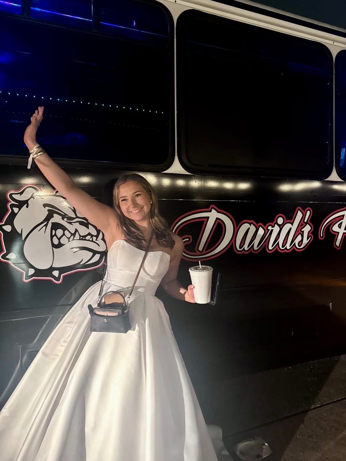 Prom guest in a white gown beside the David's party bus