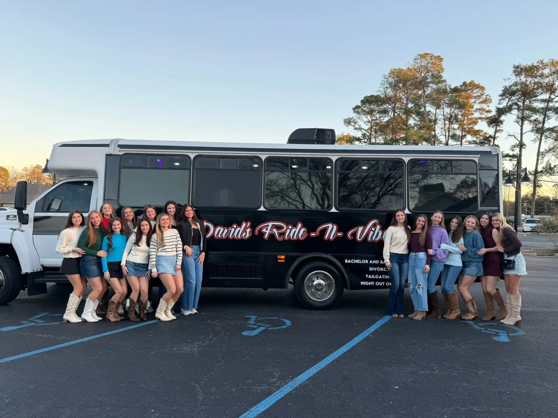 Large group of friends posing along the David's Ride-N-Vibe party bus at sunset