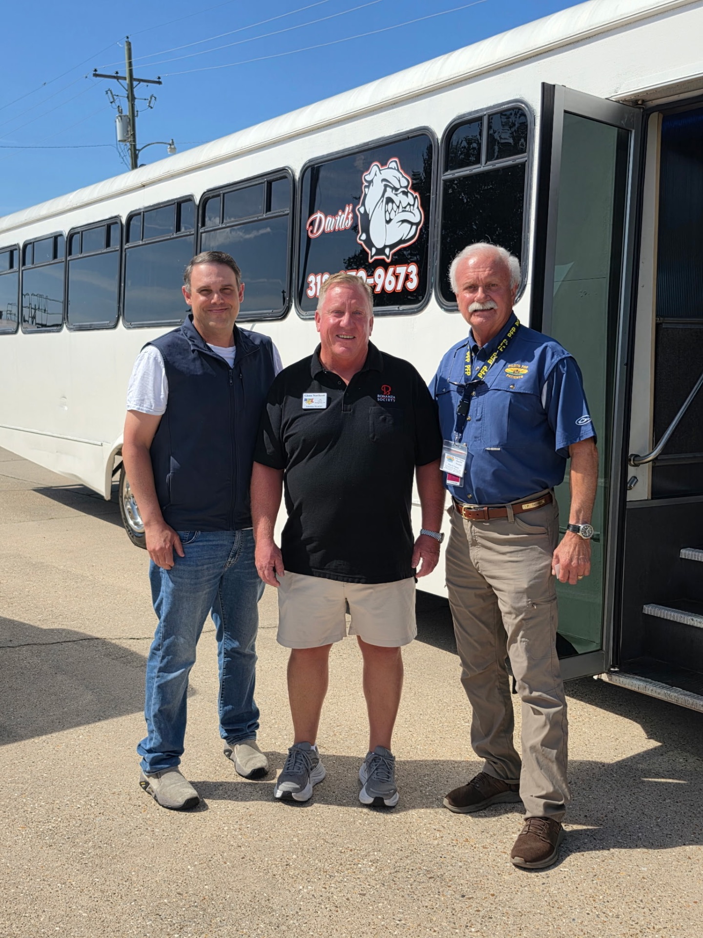 Guests standing beside the white David's Transportation Services bus with the bulldog logo