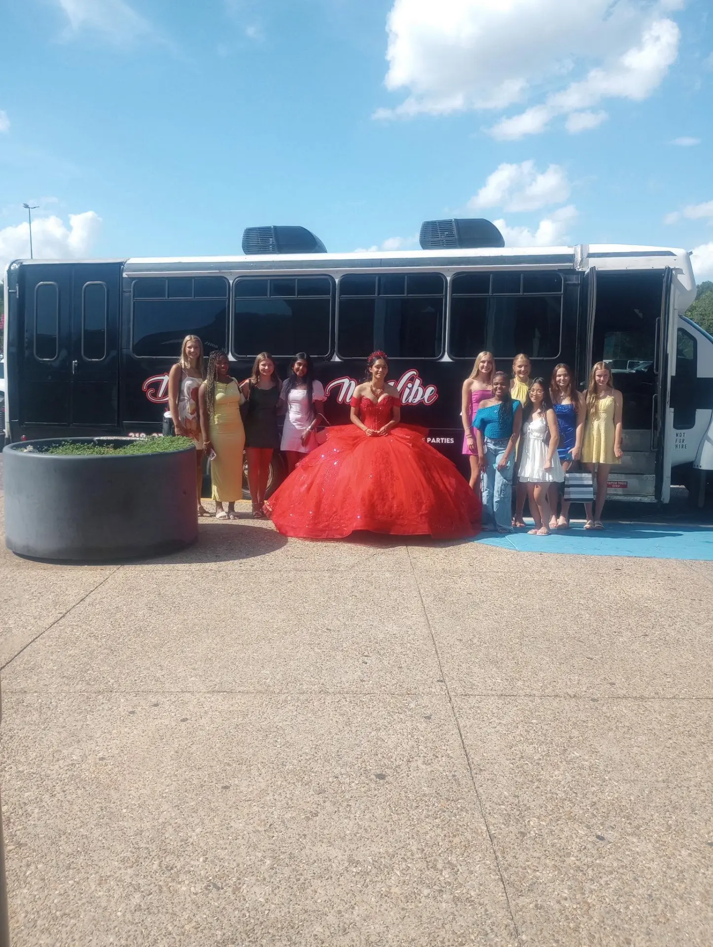 Quinceañera in a red gown with friends beside the David's Ride-N-Vibe party bus
