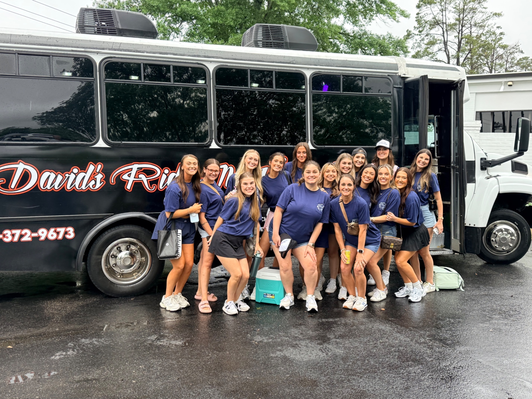 Group in matching shirts posing beside the black David's Ride-N-Vibe bus