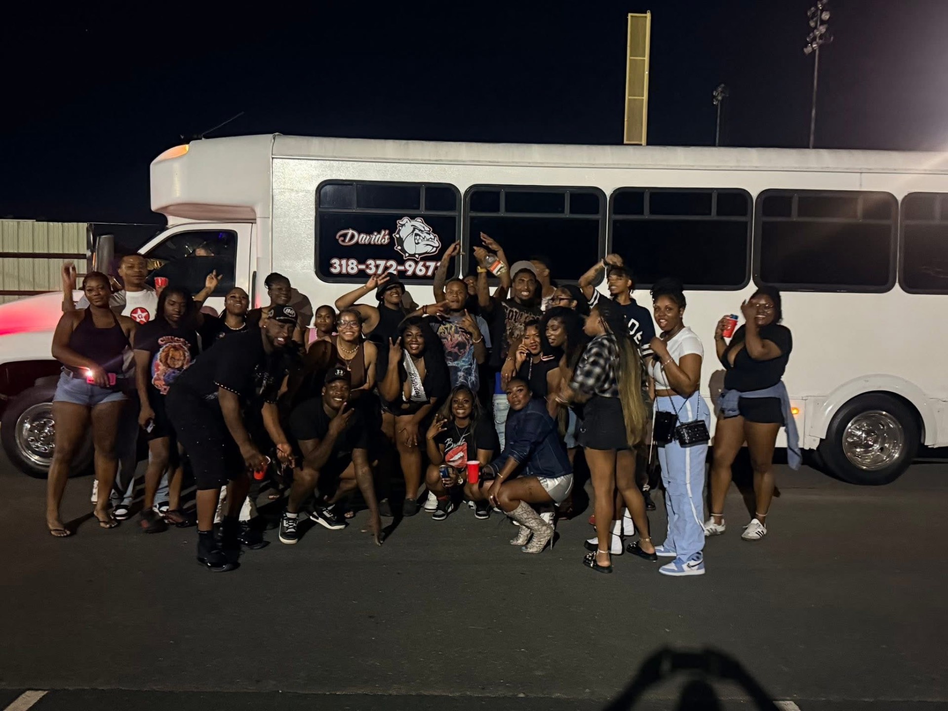 A large group posing in front of the David's Transportation Services party bus at night
